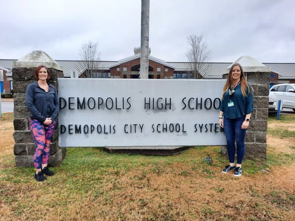 Ronda Russell and Amanda Riendeau standing next to the Demopolis High School sign.